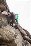 Determined man climbing a large rock face and seeing the summit and the bright sky