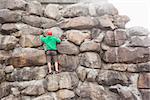 Determined man scaling a large rock face on a bright sunny day