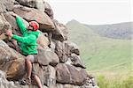 Focused man scaling a large rock face with mountains in the background