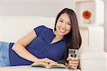 Beautiful asian girl lying on the sofa reading a novel and drinking water in living room at home