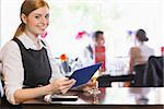 Smiling woman using tablet while holding wine glass and looking at camera in a restaurant