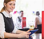 Attractive businesswoman holding tablet and wine glass and smiling at camera in a restaurant