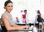 Attractive businesswoman working on laptop smiling at camera in a cafe