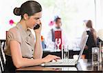 Businesswoman working on laptop while calling on phone in a restaurant