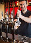 Handsome barkeeper pulling a pint of beer and smiling behind the bar