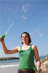 Young woman at coast playing with bubble wand