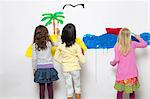 Three girls painting ocean and island on wall