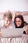 Young couple lying on bed looking at laptop