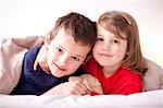 Two young children hugging under duvet