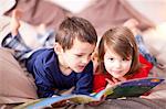 Two young children lying on bed looking at picture book