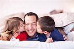 Son and daughter kissing fathers cheek under duvet