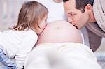 Father and daughter kissing mothers bump