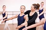 Teacher adjusting arms of shy teenage ballerina