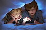 Brothers underneath duvet using digital tablet