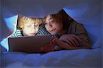 Brothers underneath duvet using digital tablet