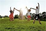 Group of young adults jumping mid air in field