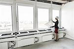 Businesswoman standing in empty unfinished office wearing hardhat and looking at plans