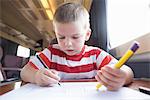 Young boy with pencil, pen and paper on train