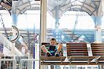 Young boy in train station waiting room playing handheld game