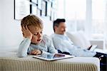 Father and son sitting on sofa using digital tablets