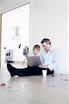 Man sitting on floor using laptop, son watching