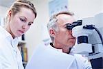 Man looking through microscope, woman looking at paperwork