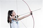 Side view of young, woman archer, aiming bow and arrow, studio shot on white background