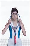 Portrait of young woman posing with tennis racket in front of face, studio shot on white background