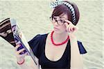 Portrait of young woman wearing horn-rimmed eyeglasses reading magazine on beach, Italy