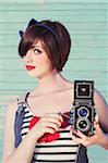Portrait of young woman looking at camera and holding vintage camera, studio shot