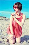 Young woman kneeling in sand on beach, wearing retro clothing, Italy