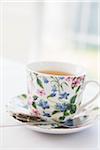 Cup of tea in pretty floral cup with saucer and used tea bag, studio shot