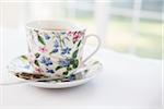 Cup of tea in pretty floral cup with saucer and used tea bag, studio shot