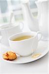 Cup of tea in porcelain white teacup with saucer, sugar bowl, teapot and plate of coconut macaroons, studio shot