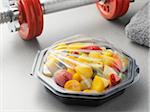 Fruit salad in plastic container with barbell, studio shot