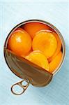 Open can of apricots, on blue background, studio shot