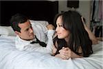 Couple laying on bed in formal wear, looking at each other