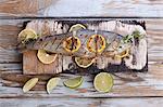 Barbecued trout with lemons and limes on a wooden board