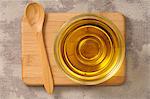 Olive oil in a glass dish on a chopping board with a wooden spoon