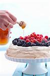 Honey being drizzled over a berry pavlova