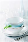 Stacked dinner bowls and plates, drinking glasses and forks