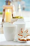 Gingerbread stars with white icing and white cups in front of candles