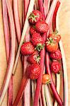 A still life featuring strawberries and stalks of rhubarb