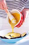 A woman pouring mustard marinade onto sliced aubergine