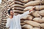 Man standing near sacks of wheat and talking on a mobile phone, Anaj Mandi, Sohna, Gurgaon, Haryana, India