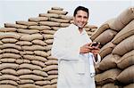 Man standing near stacks of wheat sack holding a mobile phone, Anaj Mandi, Sohna, Gurgaon, Haryana, India