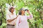 Woman looking through binoculars with her husband standing behind her, Lodi Gardens, New Delhi, India