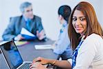 Portrait of a businesswoman working on a laptop with her colleagues discussing in the background