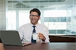 Happy businessman having coffee while using a laptop