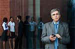 Businessman using a mobile phone with their colleagues talking in the background